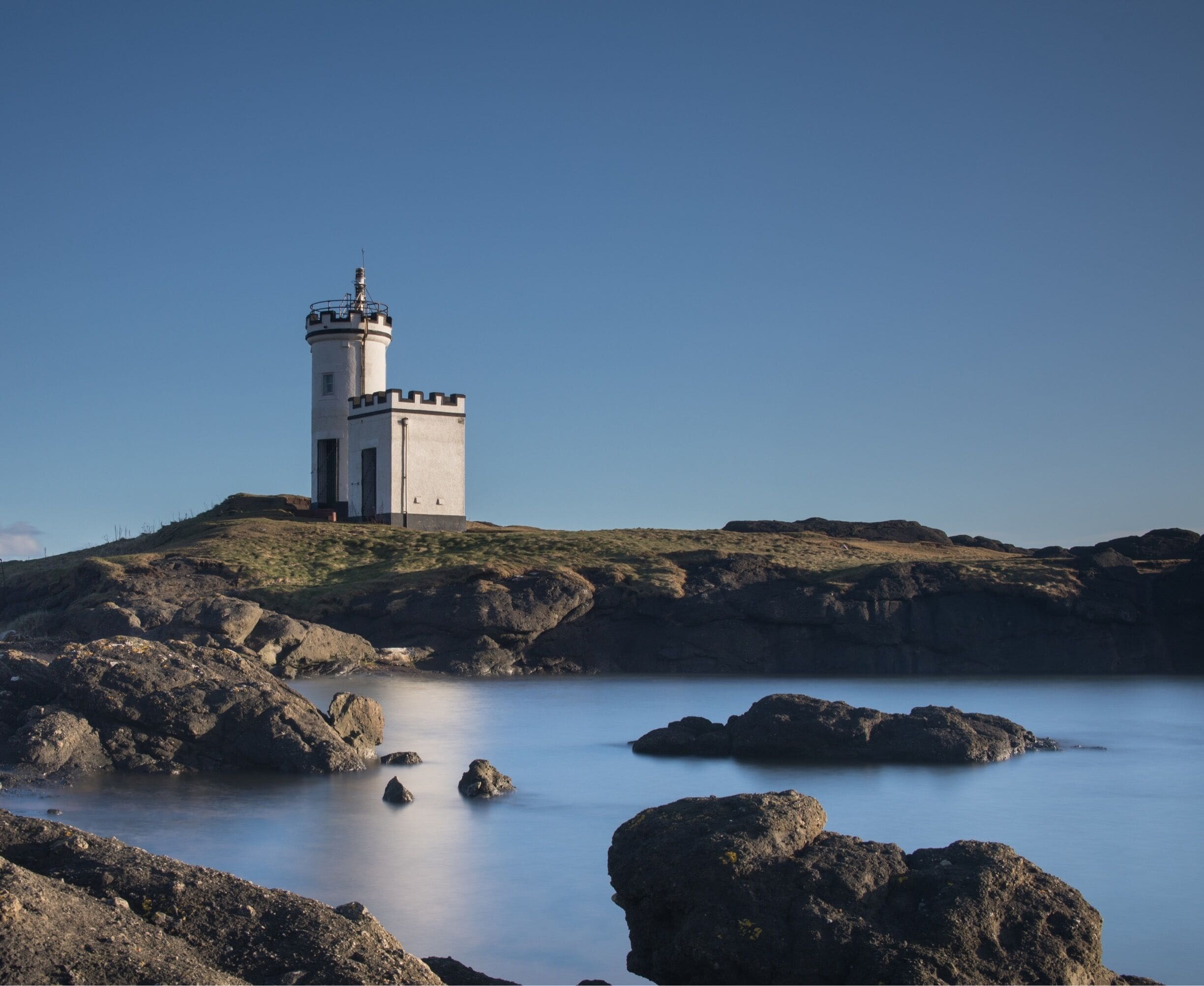 A lighthouse on a rocky island with calm water.