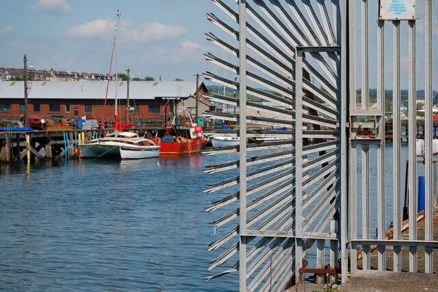 A harbor with boats docked, a metal fence, and buildings in the background.