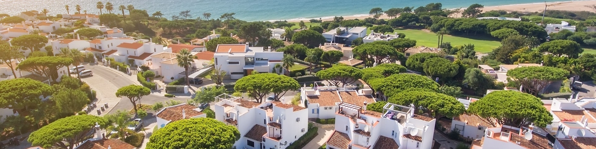 Un área residencial costera con casas blancas, árboles verdes y una playa al fondo.