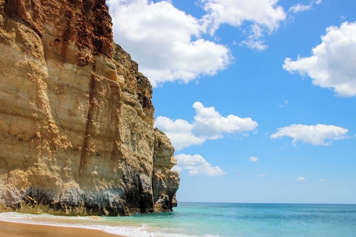 A coastal cliff with clear blue waters and a sandy beach.