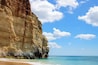 A coastal cliff with clear blue waters and a sandy beach.
