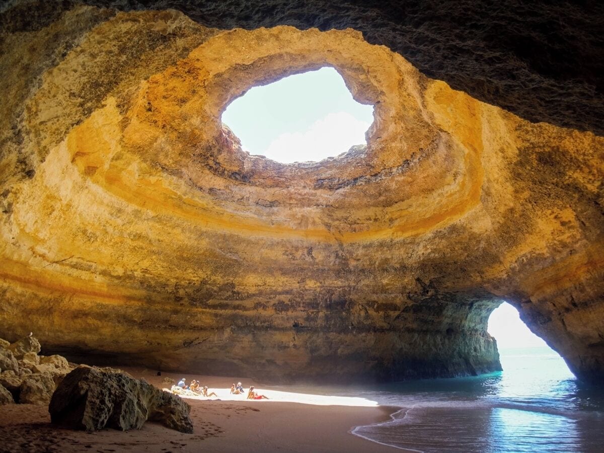 A large cave with a circular opening and a beach at the base.
