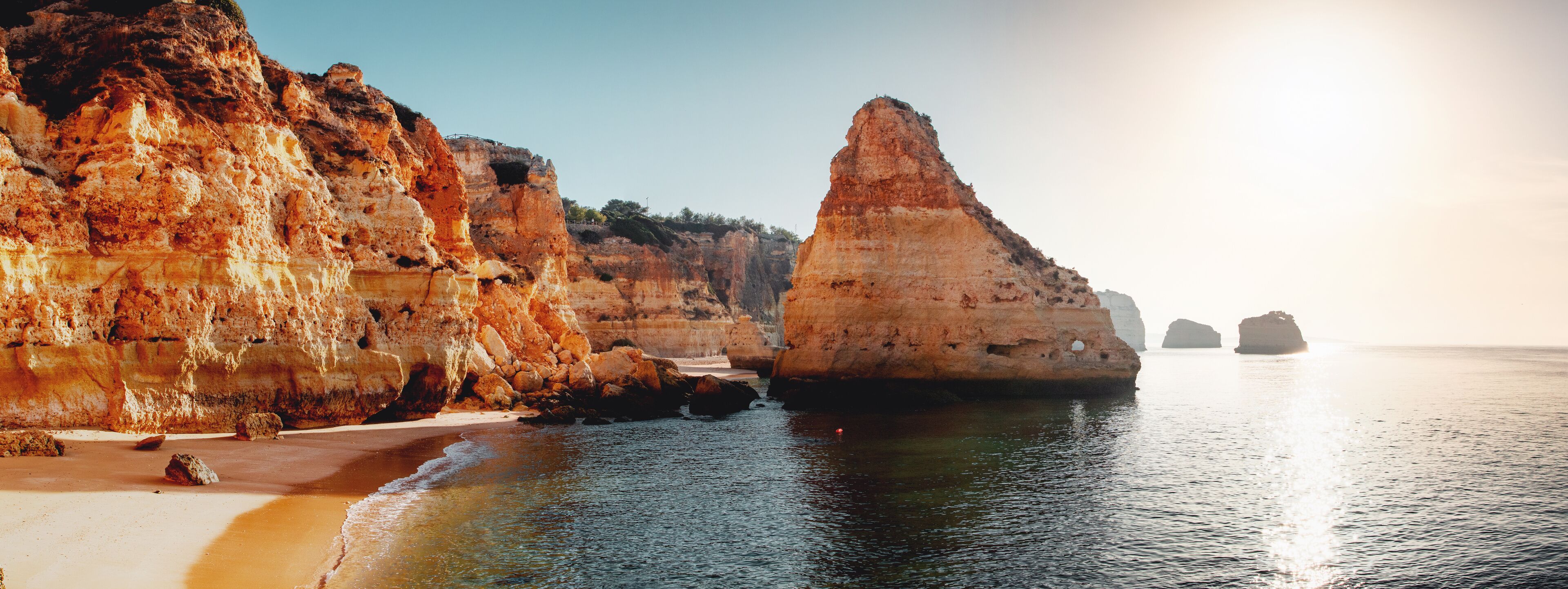 A coastal landscape with towering cliffs, a sandy beach, and calm sea.