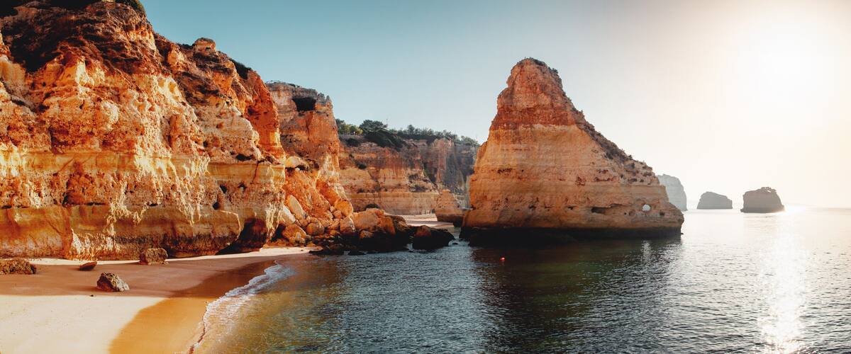 A coastal landscape with towering cliffs, a sandy beach, and calm sea.