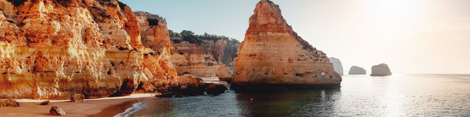 A coastal landscape with towering cliffs, a sandy beach, and calm sea.