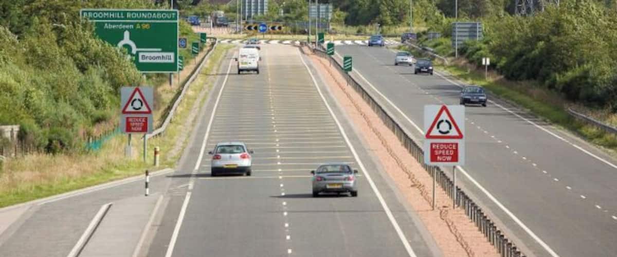 A multi-lane highway with road signs, including directions to Broadhill and Aberdeen.