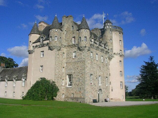 A large castle with multiple towers and turrets, surrounded by a well-maintained lawn.