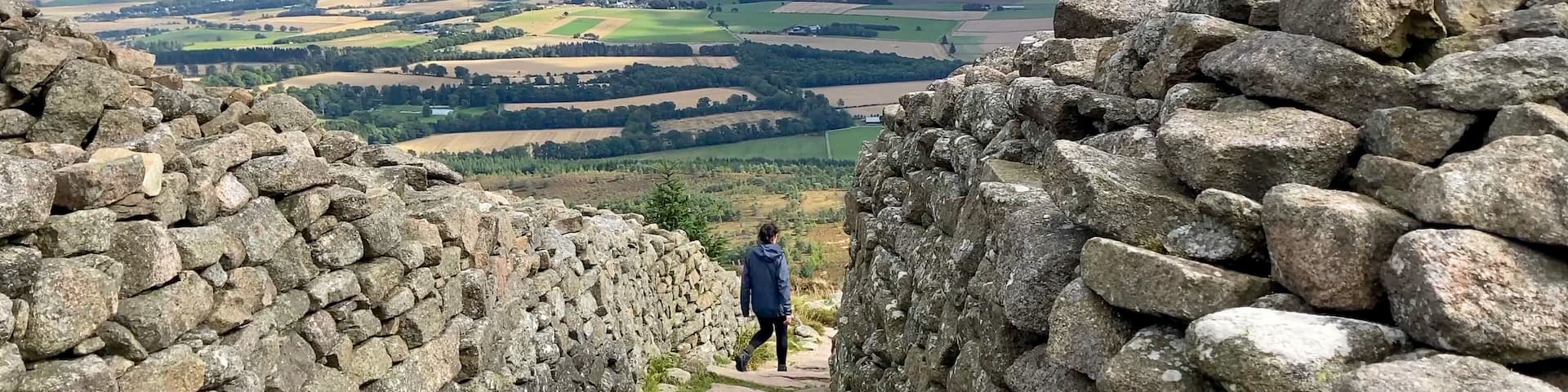 A female hiker walks down the stone steps of the ancient hill fort on top of Mither Tap in the Bennachie Mountain Range - Nr Inverurie, Aberdeenshire, Scotland, UK