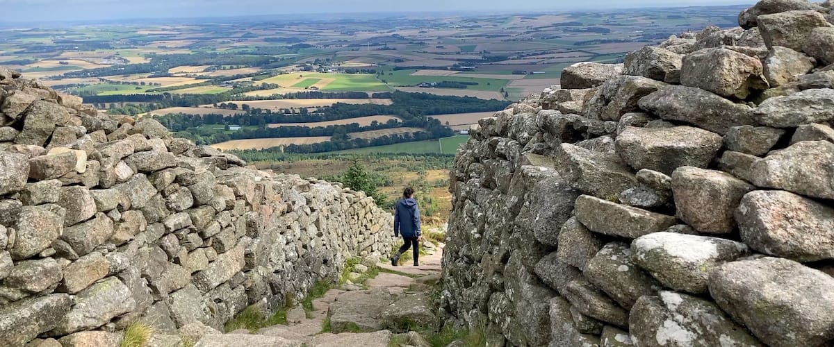 A stone wall with a person walking through a rural landscape.