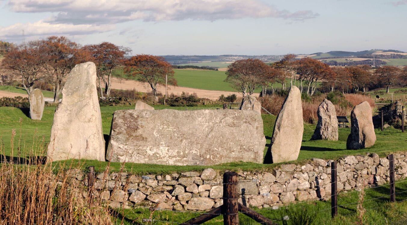 A stone circle with standing stones and a large stone slab in a grassy field.