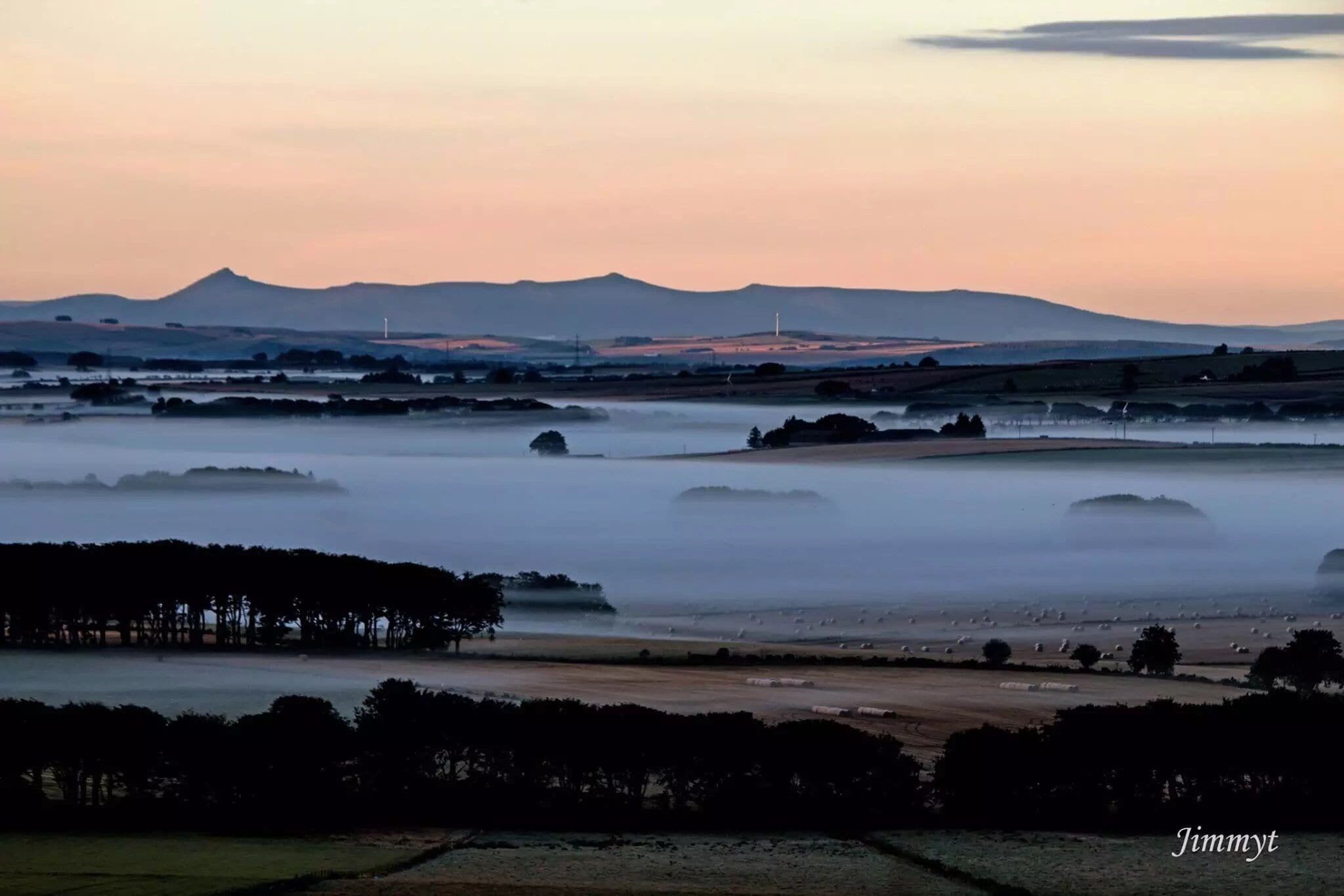 A misty landscape with rolling hills, a distant mountain, and scattered trees.