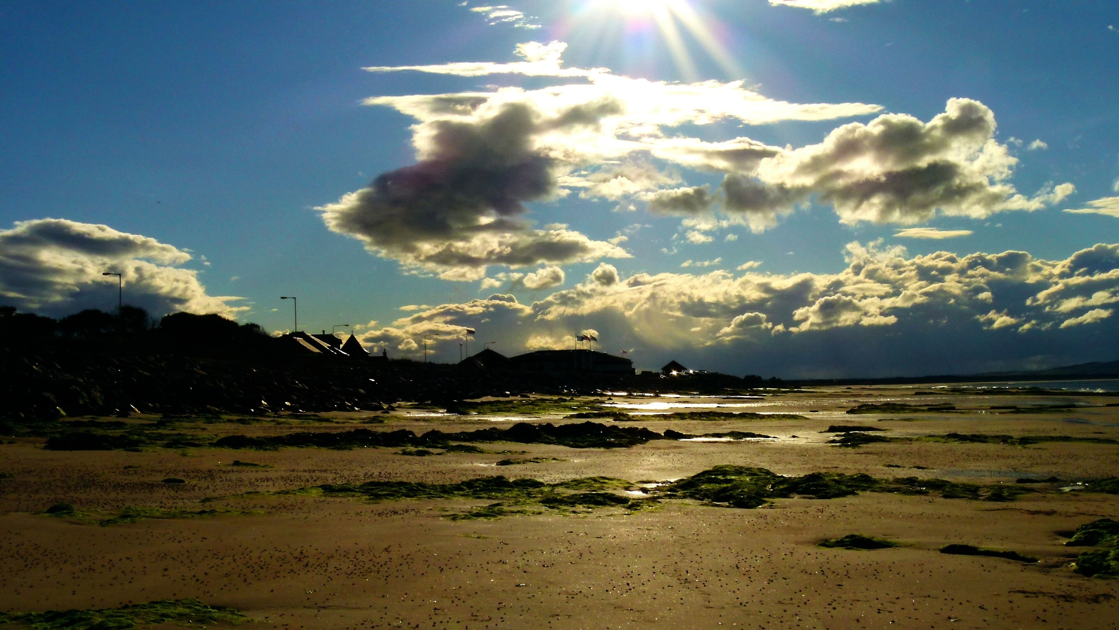 A beach with scattered rocks and a distant view of a city skyline under a partly cloudy sky.