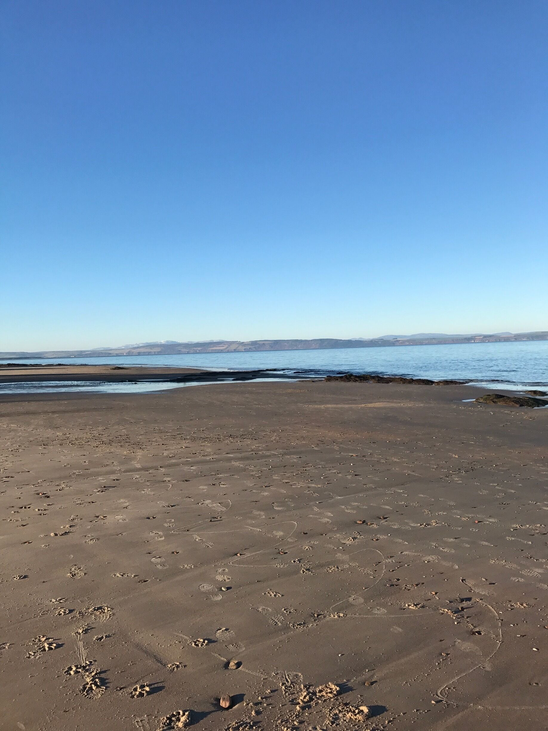 A sandy beach with footprints and a clear blue sky.