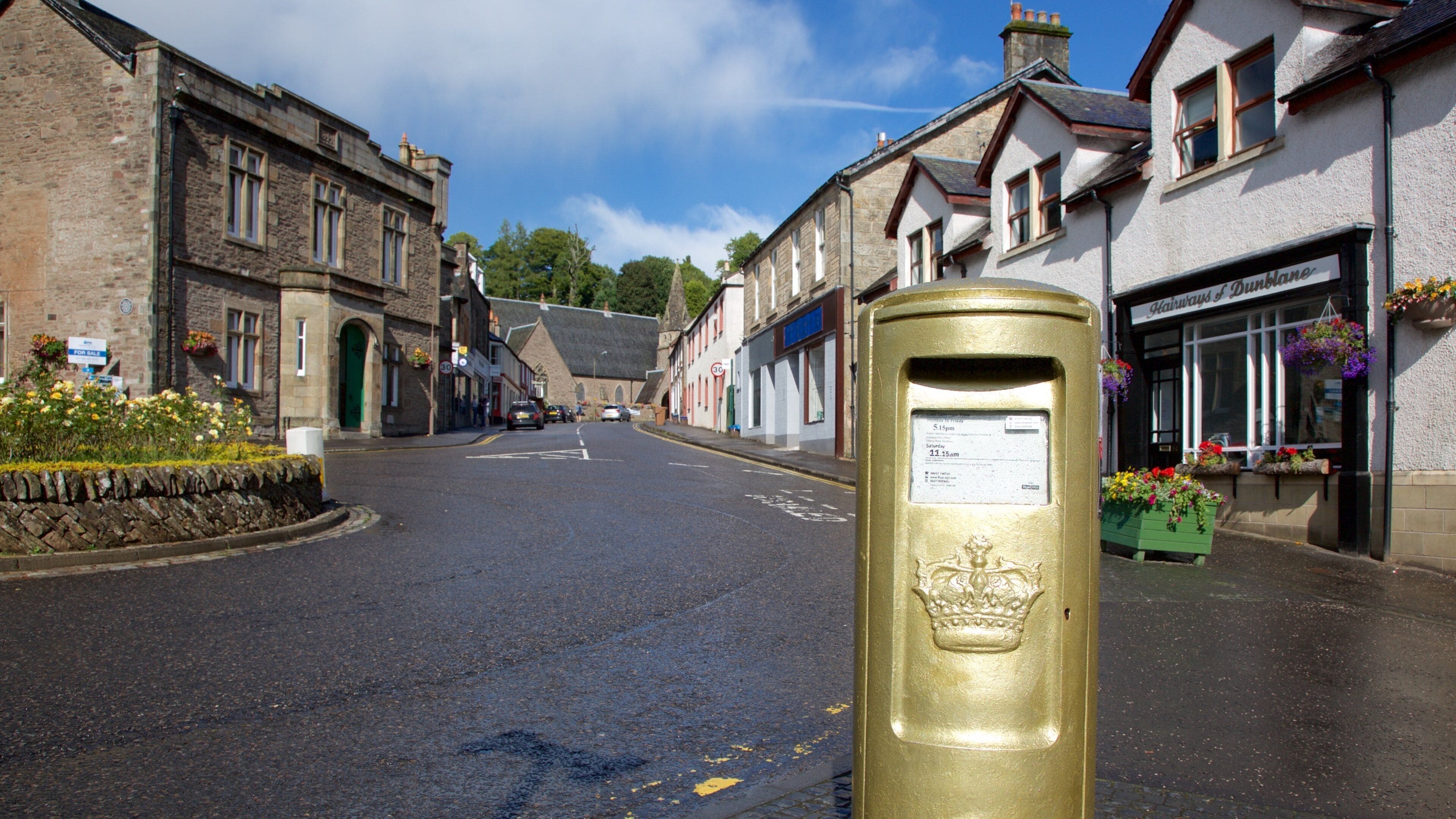 A street with stone buildings, a gold post box, and flower boxes on the right.