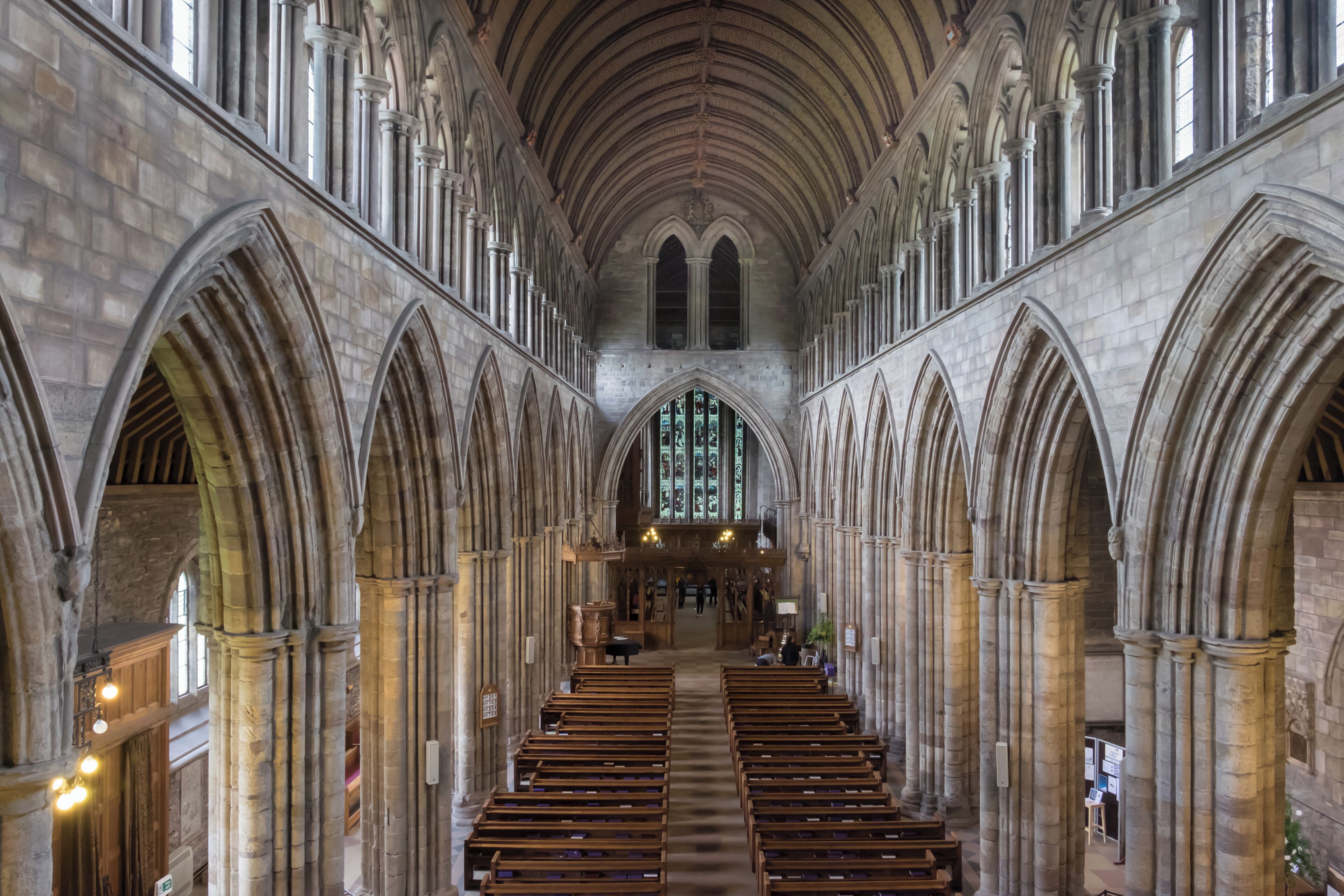 A cathedral interior with high vaulted ceilings, arched windows, and rows of pews.