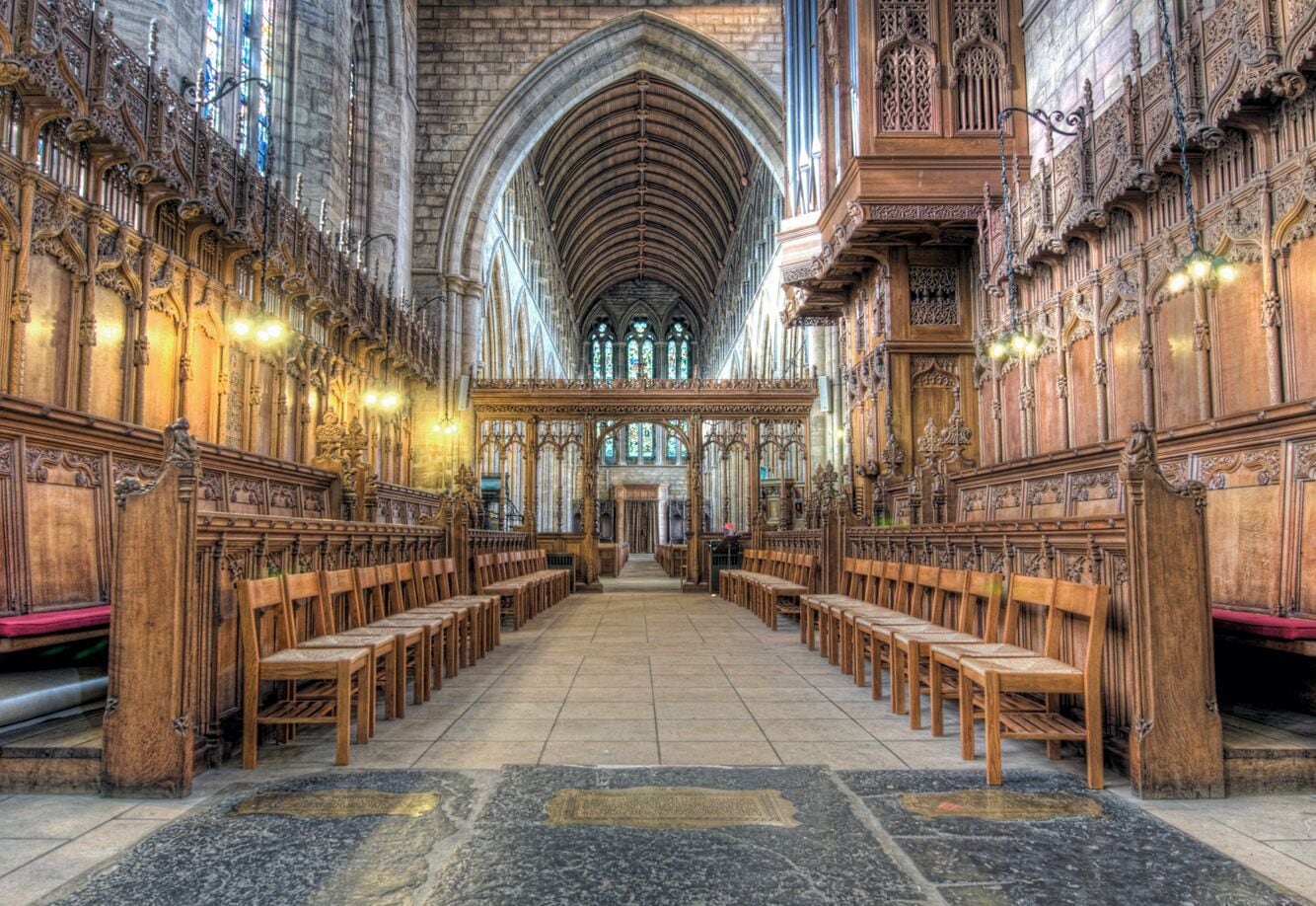 A cathedral interior with wooden pews, a stone floor, and Gothic architecture.