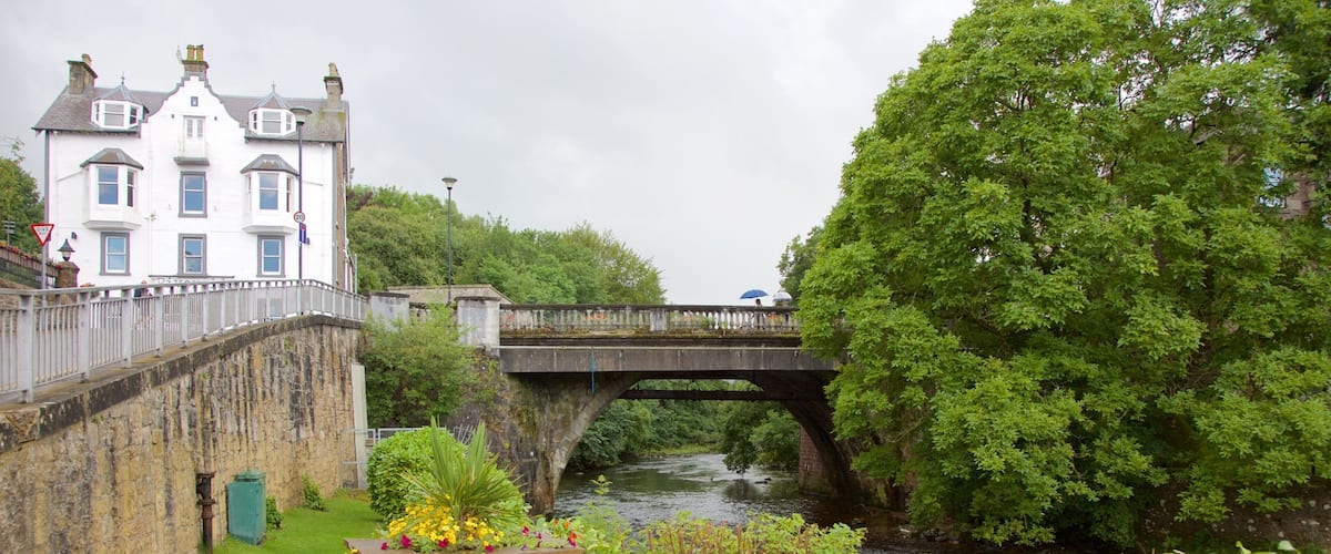A stone bridge over a river, surrounded by lush greenery and a white building with a balcony.