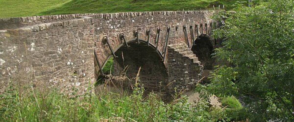 A stone bridge over a water channel, surrounded by lush green hills.