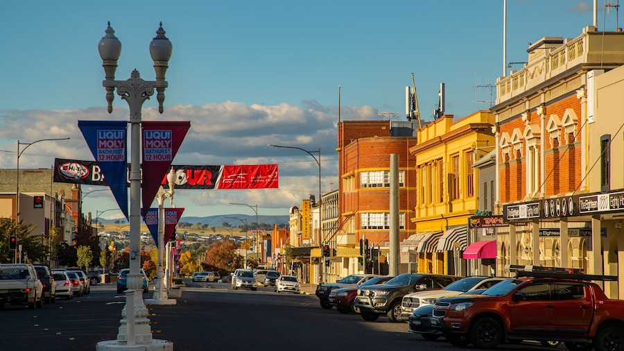 A street lined with parked cars, vintage buildings, and various commercial signs.