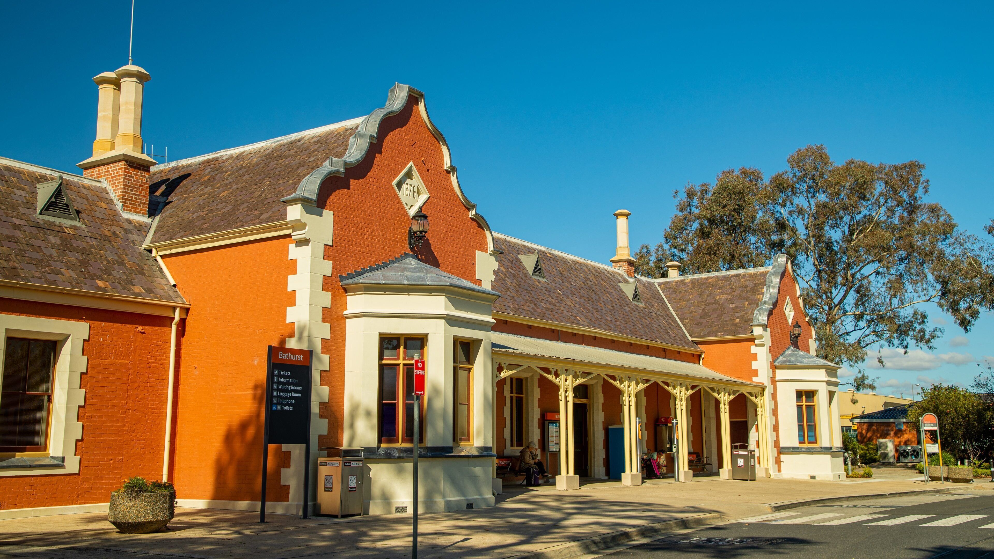 A historic building with a red brick facade, a white entrance, and a signboard listing amenities like tickets, information, and waiting rooms.
