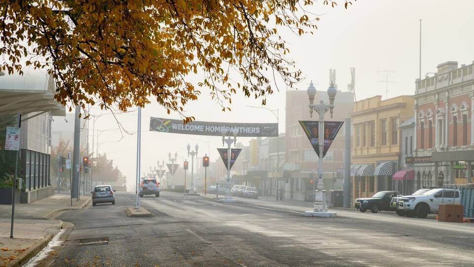 Een straat met herfstbladeren, een verwelkomingsbord en historische gebouwen.