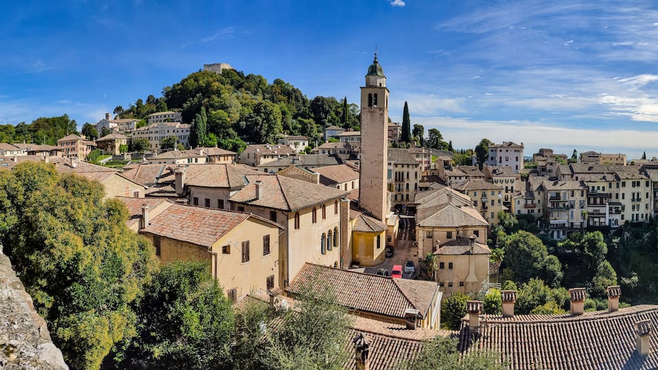 A historic town with a prominent church tower, terracotta-roofed buildings, and a castle on a hill.