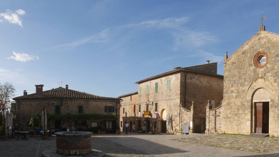 A cobblestone square with historic buildings, a fountain, and a church with a bell tower.