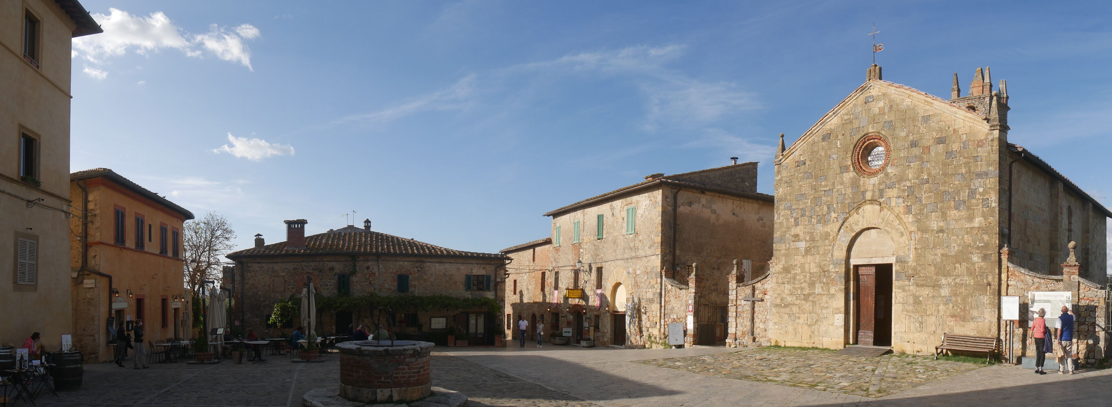 A cobblestone square with historic buildings, a fountain, and a church with a bell tower.
