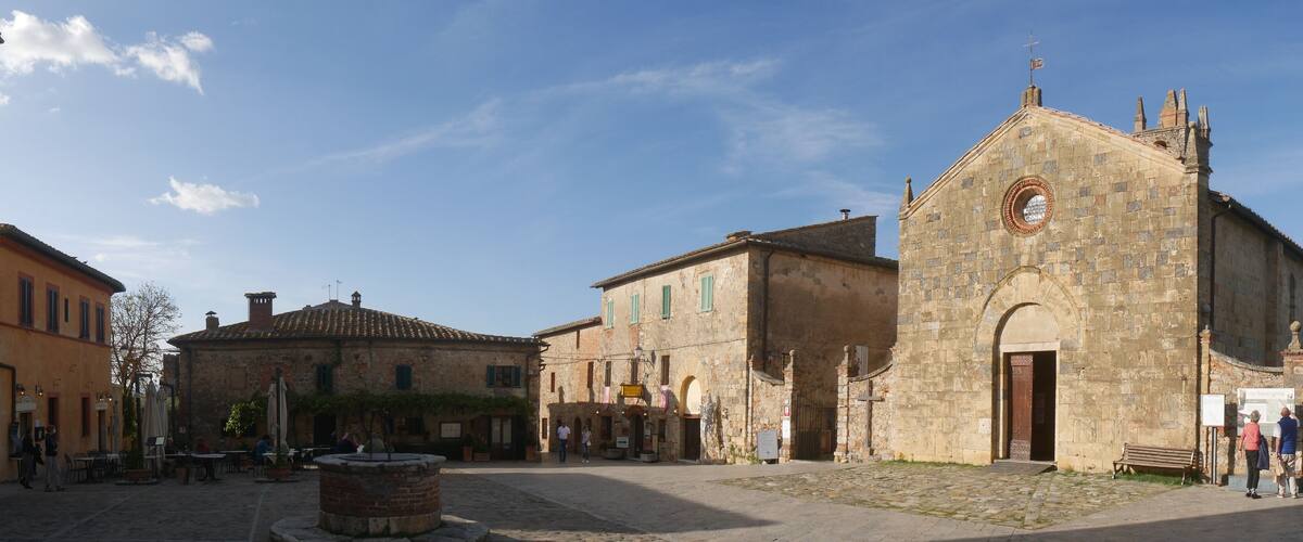 A cobblestone square with historic buildings, a fountain, and a church with a bell tower.