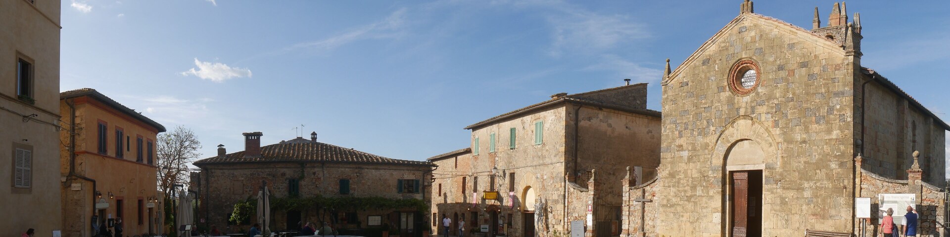 A cobblestone square with historic buildings, a fountain, and a church with a bell tower.
