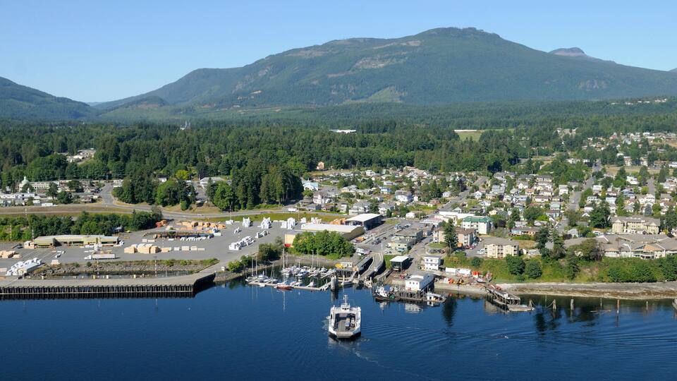 A coastal town with a marina, surrounded by forested hills and mountains.
