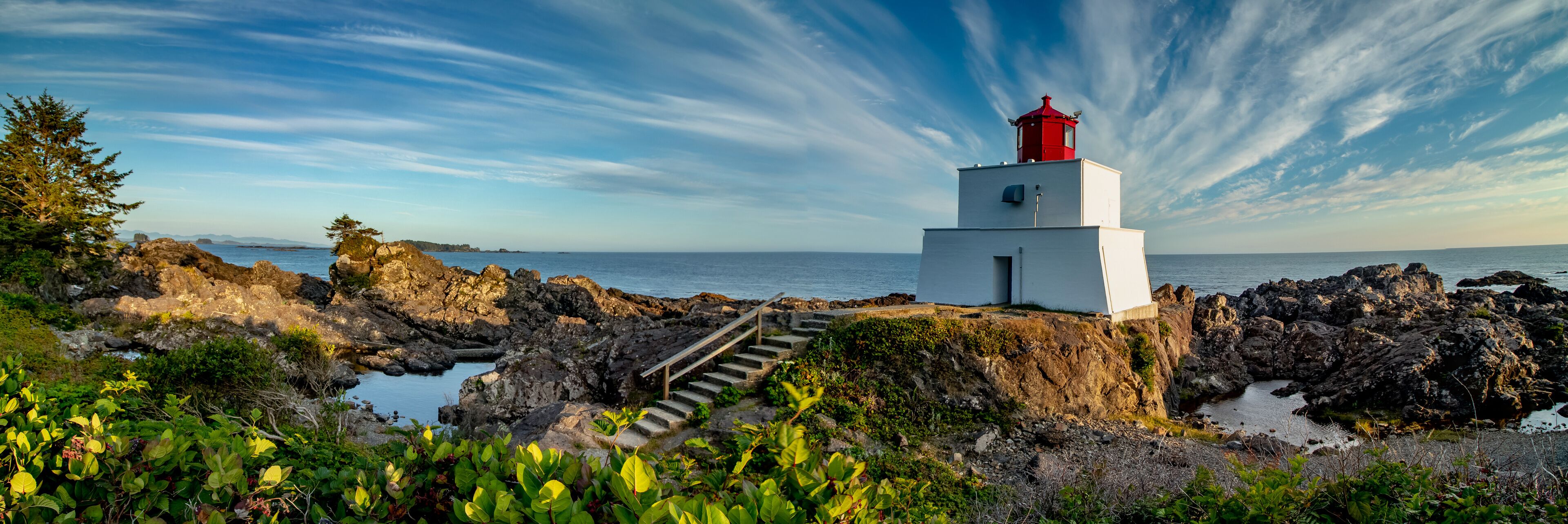 Um farol numa costa rochosa, com céu claro e mar calmo.