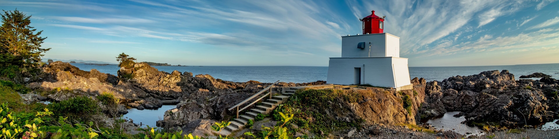 Um farol numa costa rochosa, com céu claro e mar calmo.