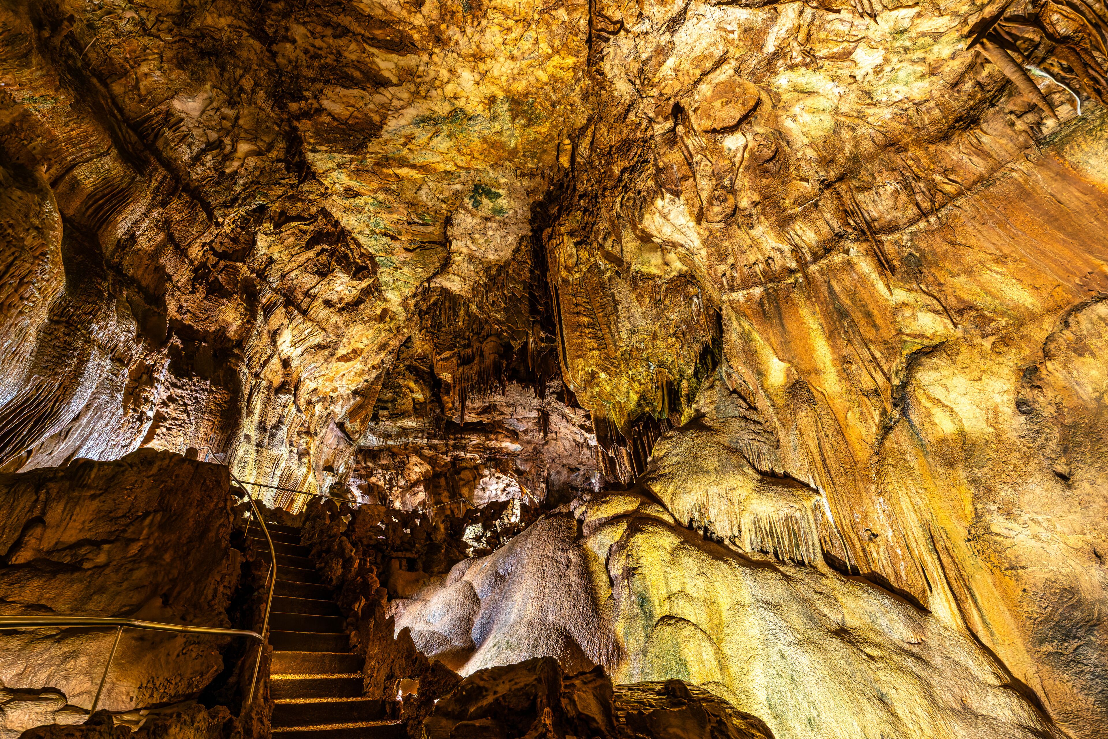 A cave with natural rock formations, a staircase, and a series of stalactites and stalagmites.