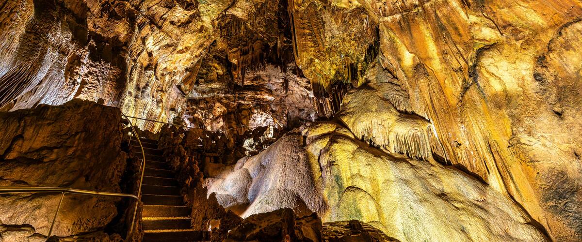 A cave with natural rock formations, a staircase, and a series of stalactites and stalagmites.