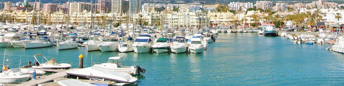 Benalmadena Puerto Marina sport port, a view to piers with white modern luxury sport yachts, Mediterranean sea and mountains and cloudy sky at the background. Spain winter relax vacation concept.
