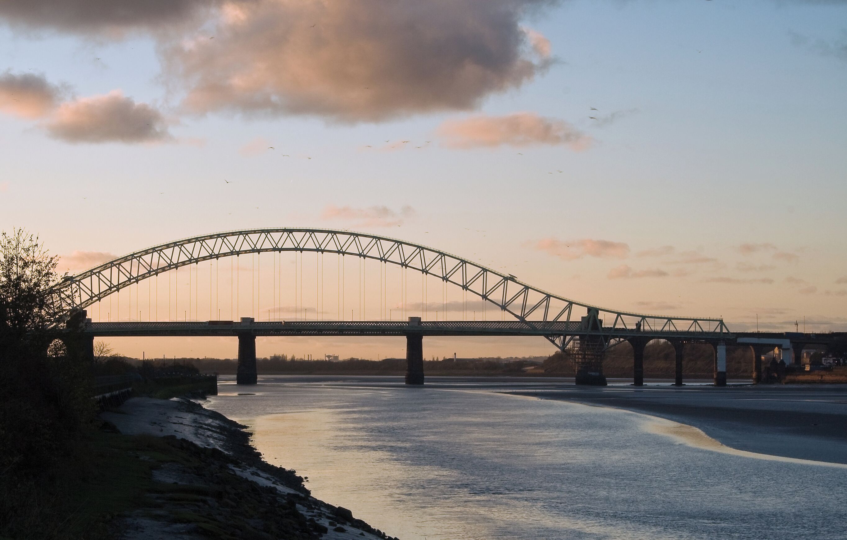 A large suspension bridge over a river at sunset.