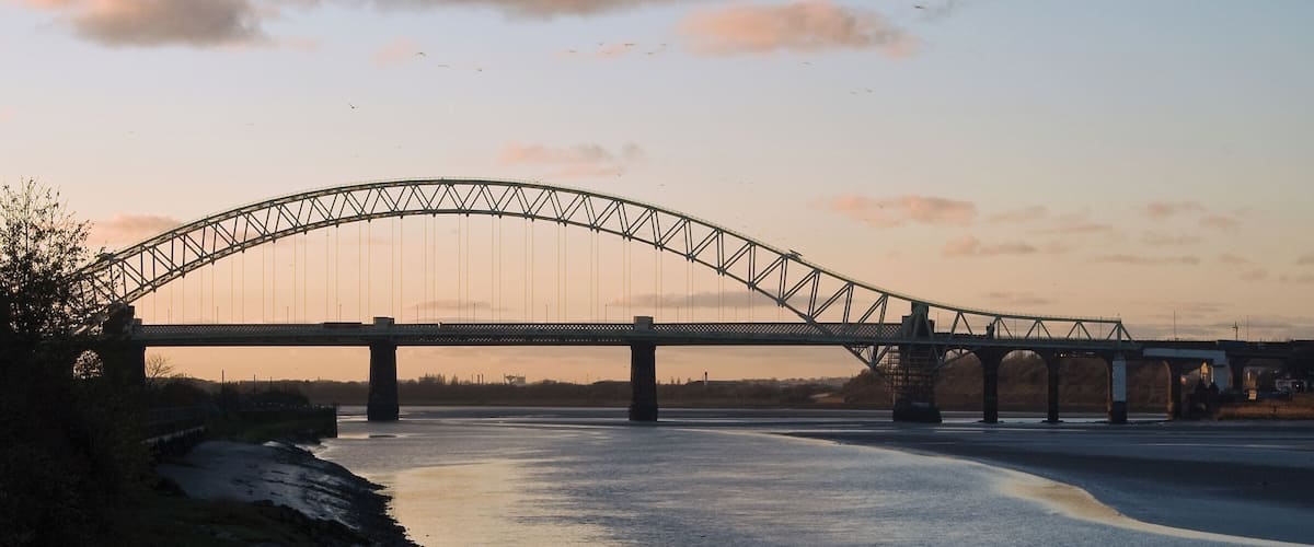 A large suspension bridge over a river at sunset.