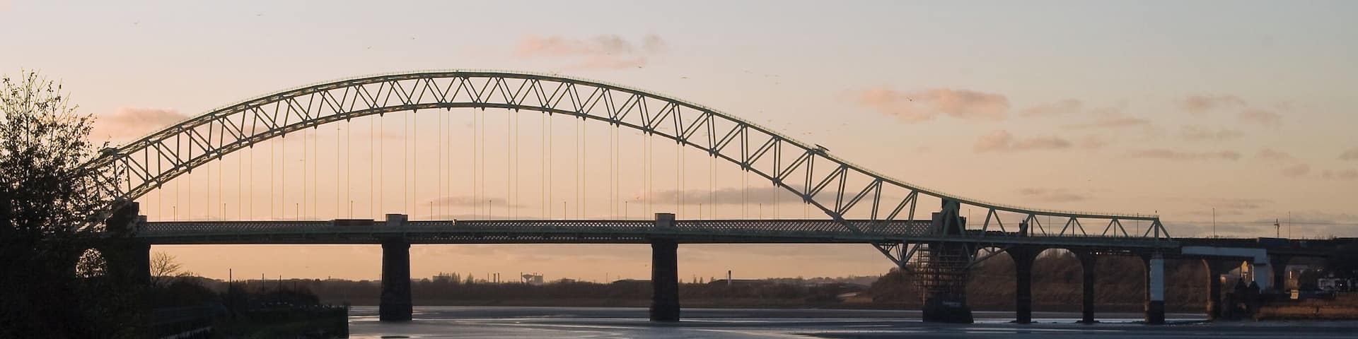 A large suspension bridge over a river at sunset.