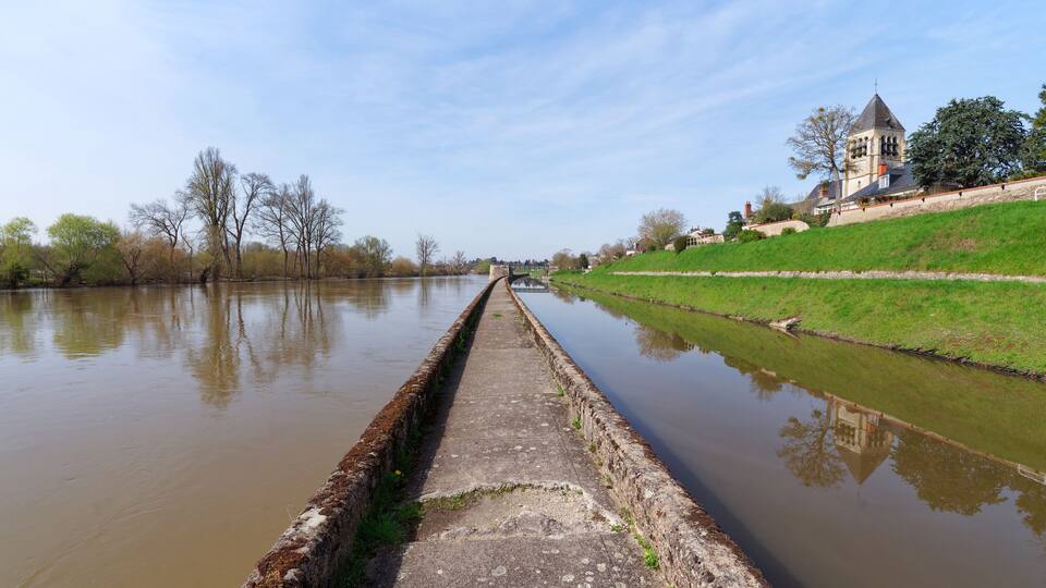 A canal with a bridge, a church, and a grassy embankment.