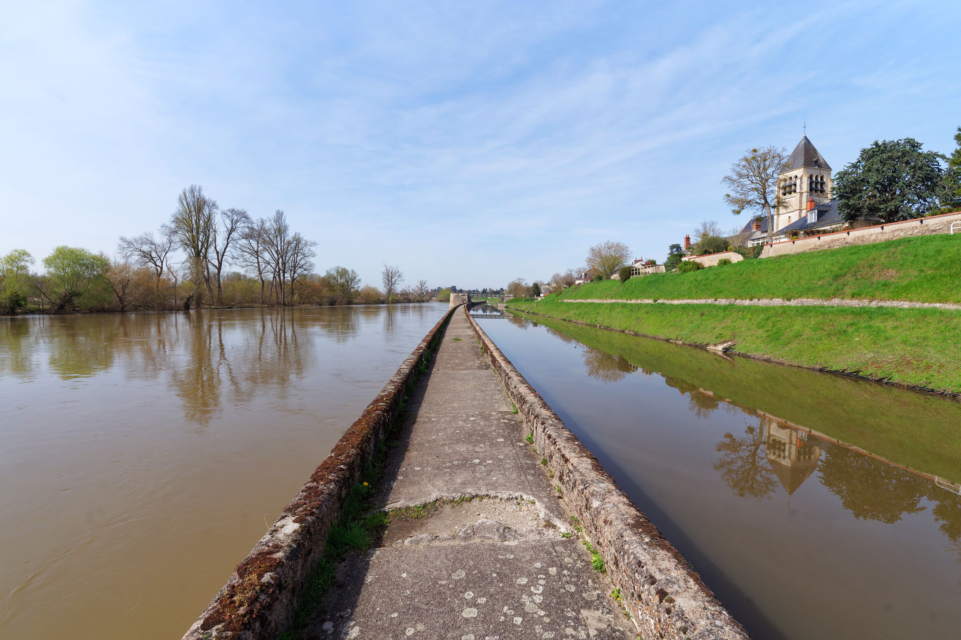 A canal with a bridge, a church, and a grassy embankment.
