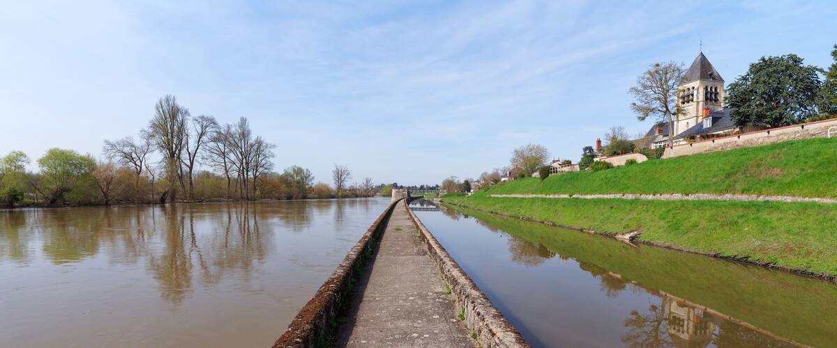 A canal with a bridge, a church, and a grassy embankment.