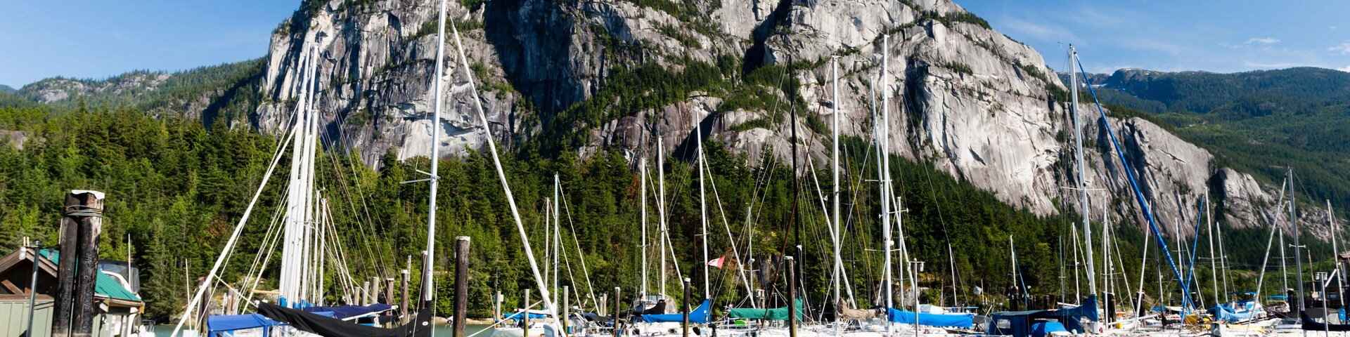 Marina con barcos amarrados en aguas tranquilas, un acantilado rocoso grande al fondo y un cielo azul despejado.