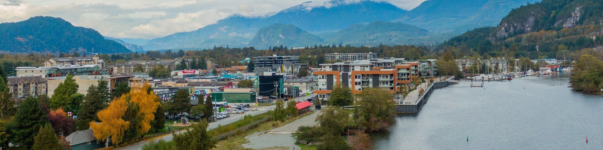 A riverside town with buildings, a dock, and mountains in the background.