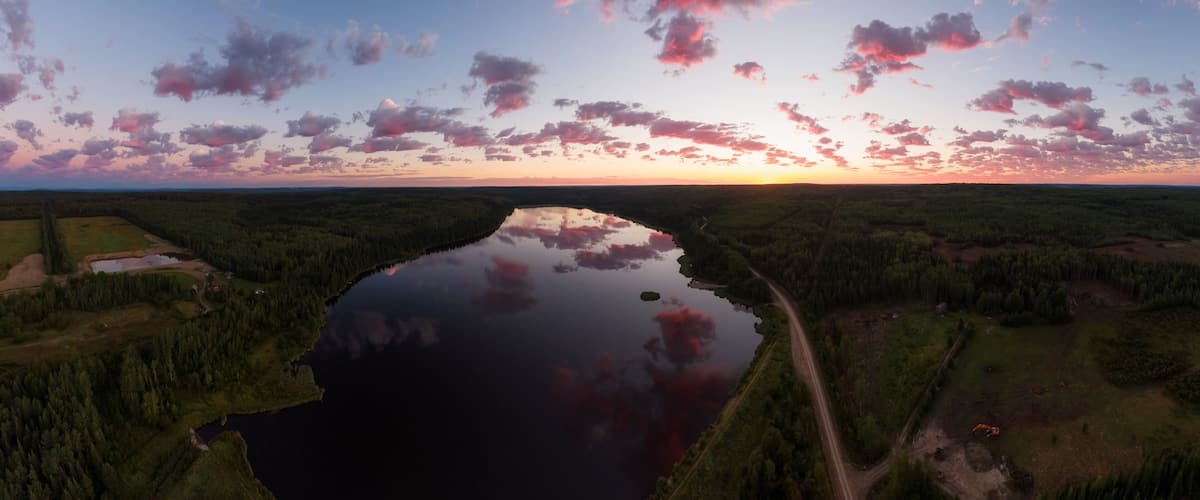 A river reflecting the sunset, surrounded by dense forest and a clear sky.