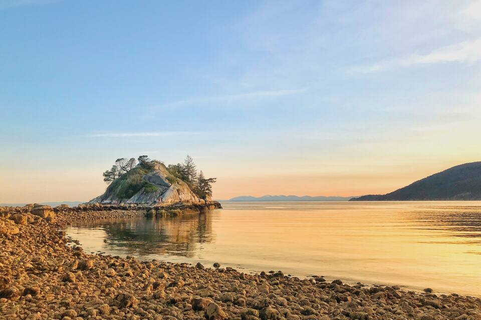 A rocky shoreline with a prominent rock formation surrounded by trees, overlooking a calm body of water.
