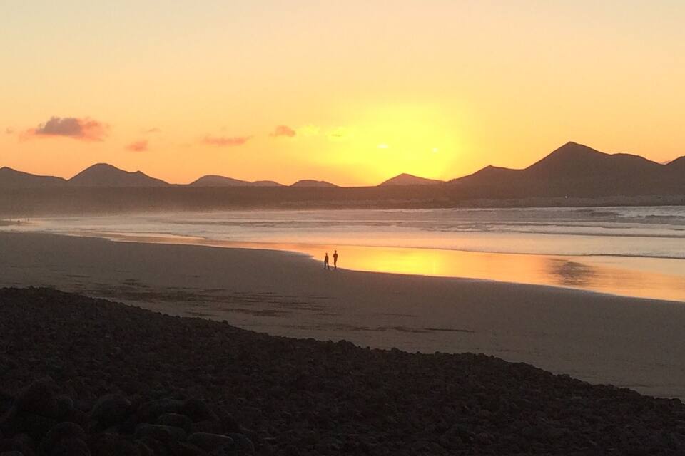 A beach at sunset with mountains in the background.
