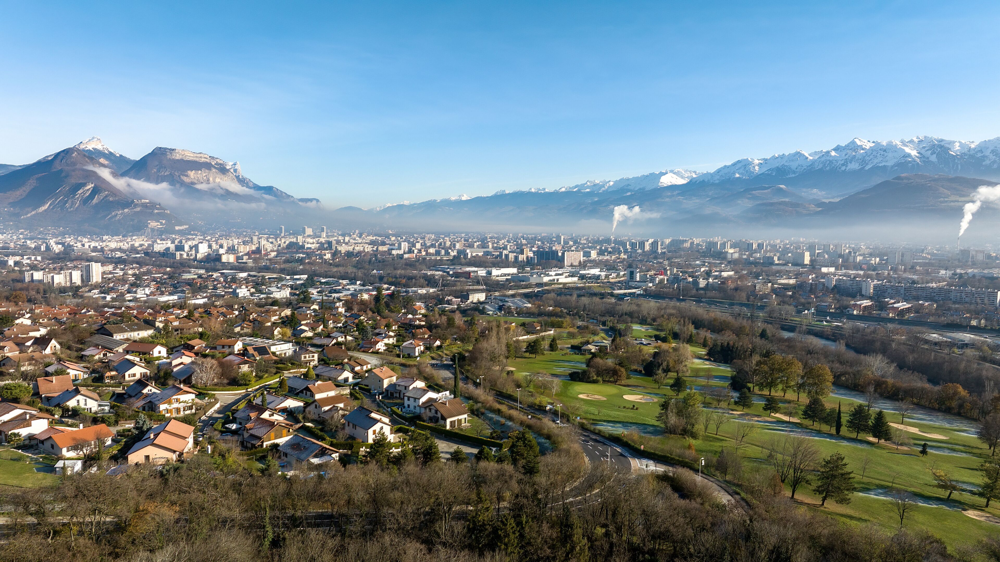 A cityscape with a mountain range in the background, a river, and residential areas.