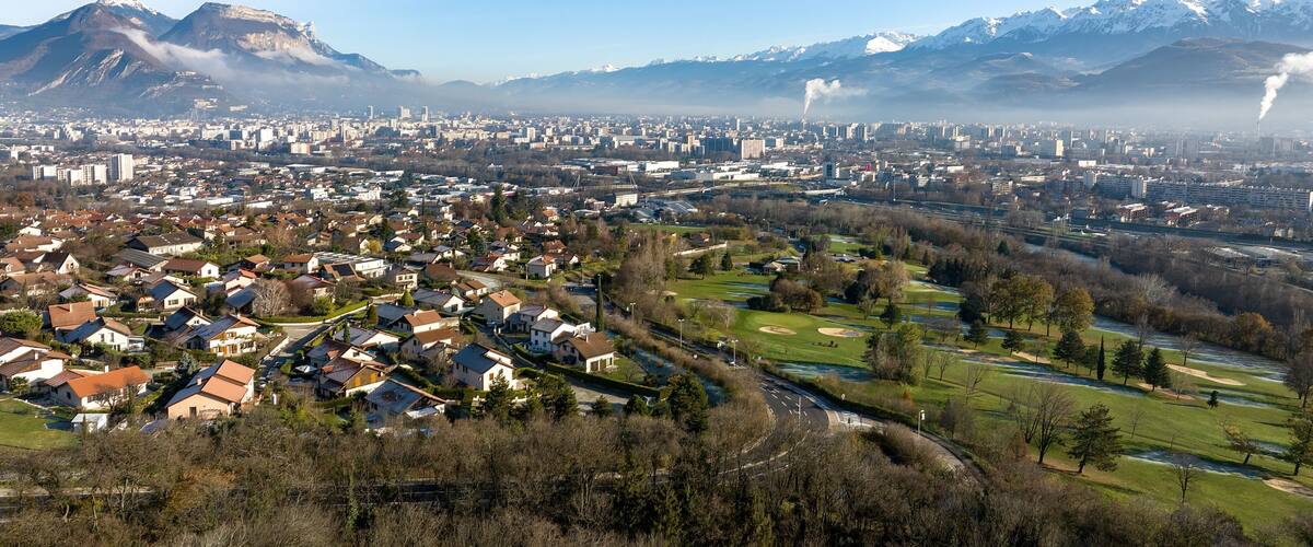A cityscape with a mountain range in the background, a river, and residential areas.