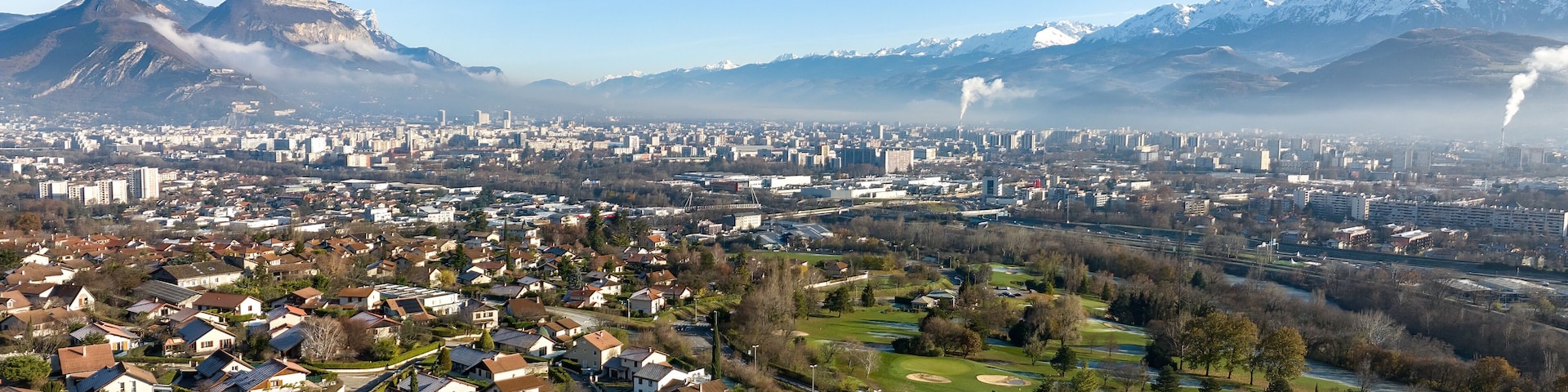 A cityscape with a mountain range in the background, a river, and residential areas.